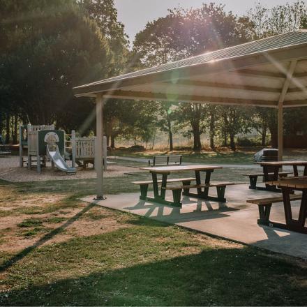 Portage park playground area. There is playground equipment in the background and a gazebo covering a few picnic tables in the foreground.