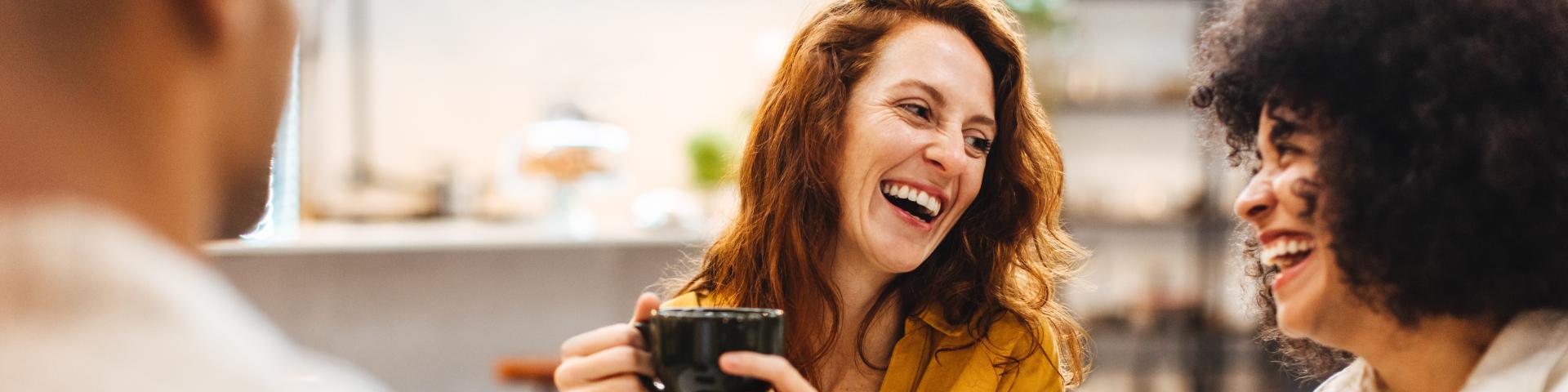 two women laughing with coffee in hand