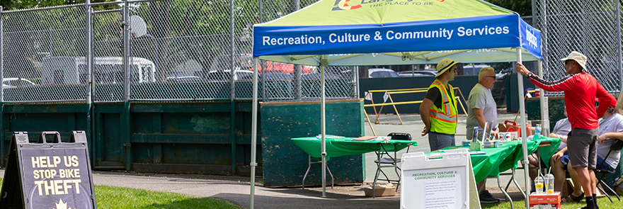 Langley City Pop Up Tent with multiple people standing under it; this tent is for the bike valet, a free service to safely secure your bike at the event.