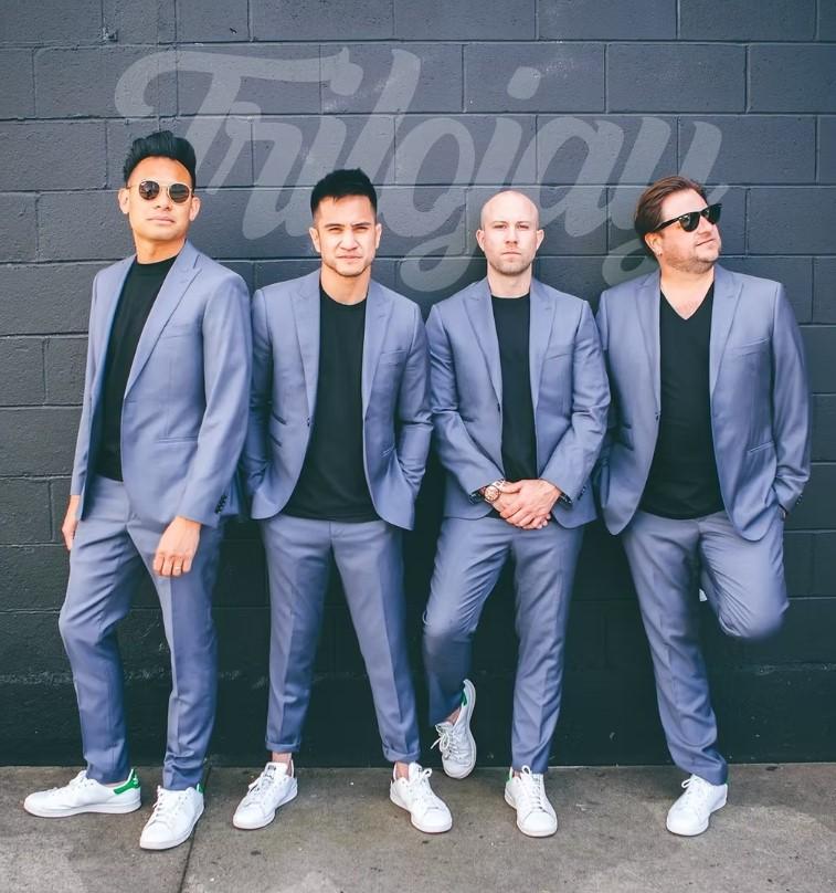 Four males standing against a wall; members of the band Trilojay